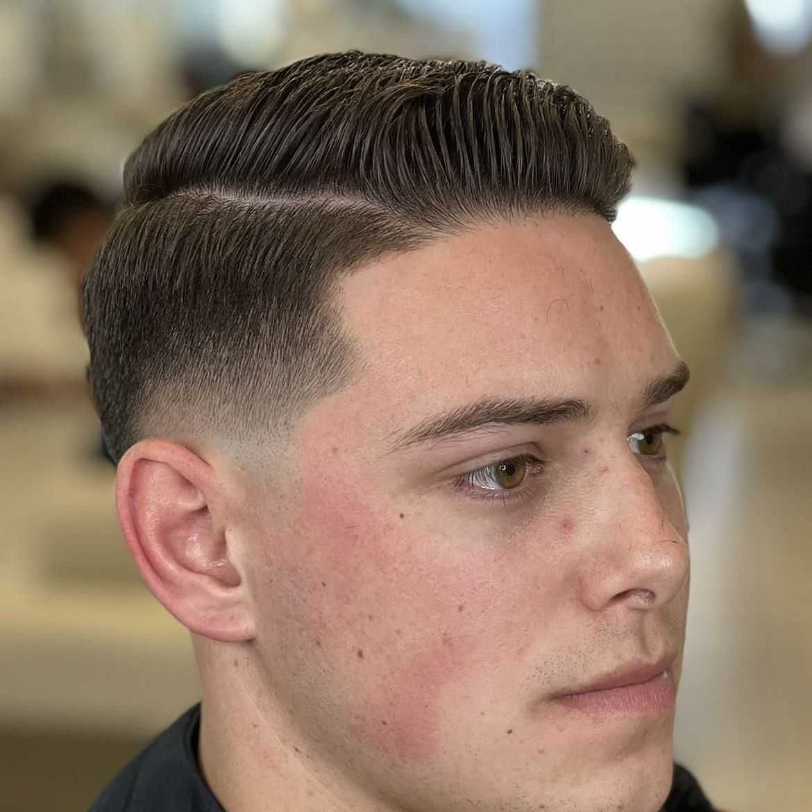 Man with a neat comb over haircut and fade sides.
